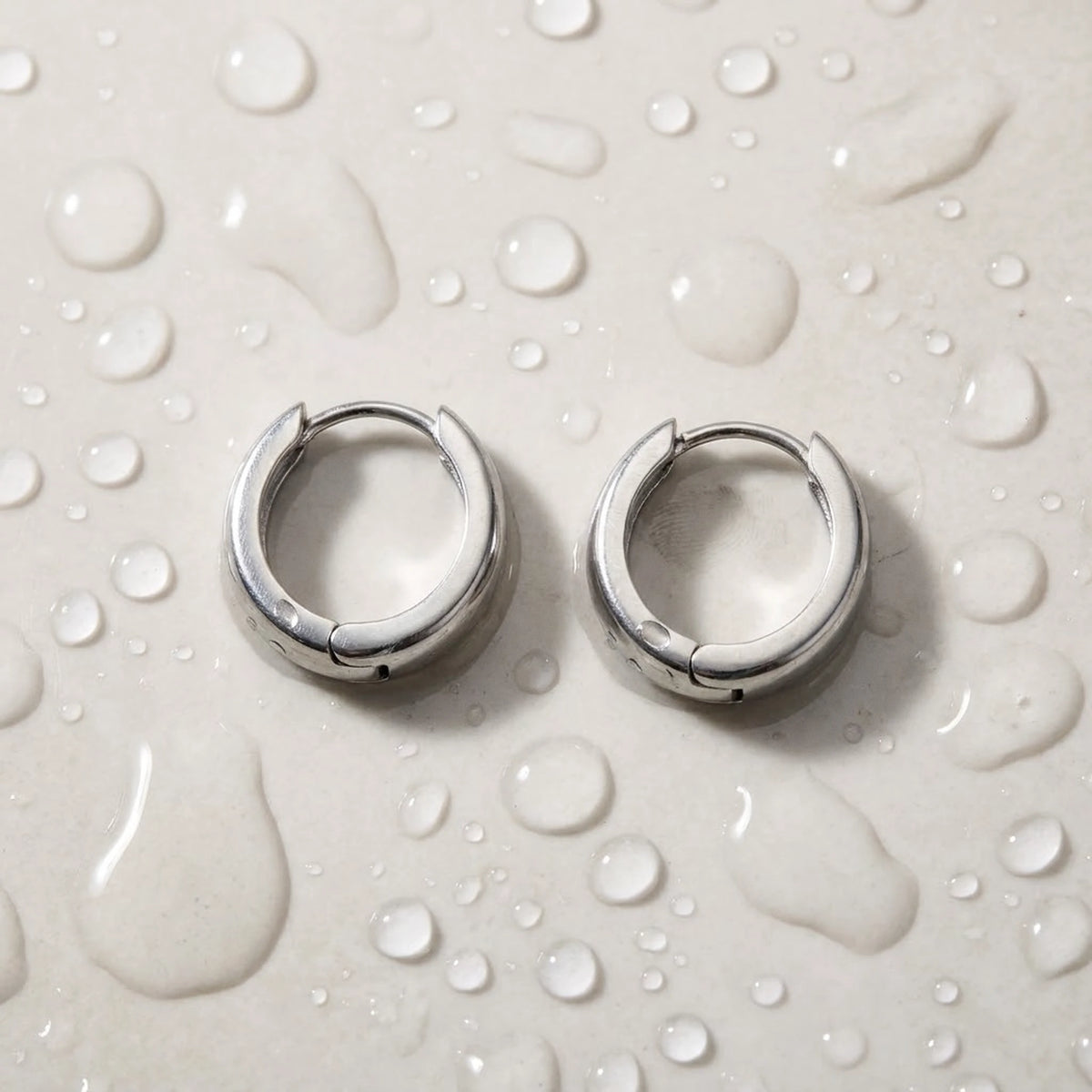 Silver tone stainless steel chunky dome hoop earrings, still life on a wet surface, waterproof | SKU: AUR-CHKDOM-S