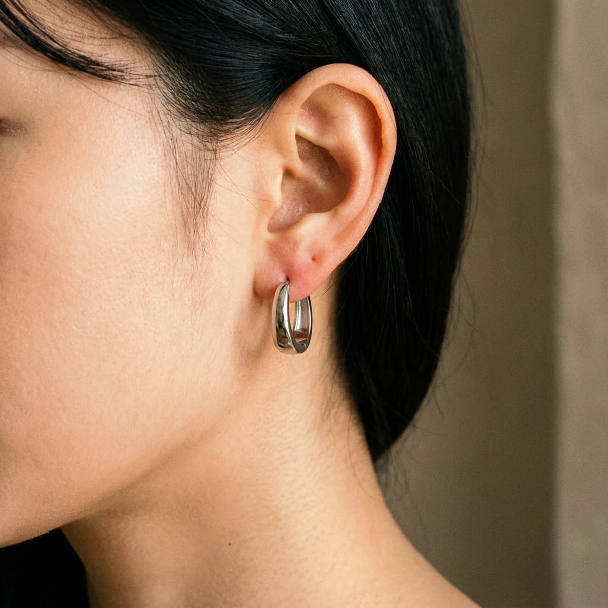 Silver tone stainless steel chunky dome hoop earrings, worn close up on the ear