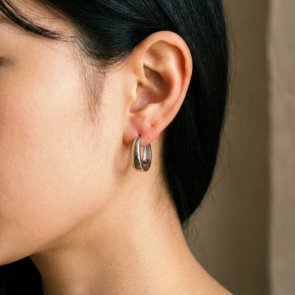 Silver tone stainless steel chunky dome hoop earrings, worn close up on the ear