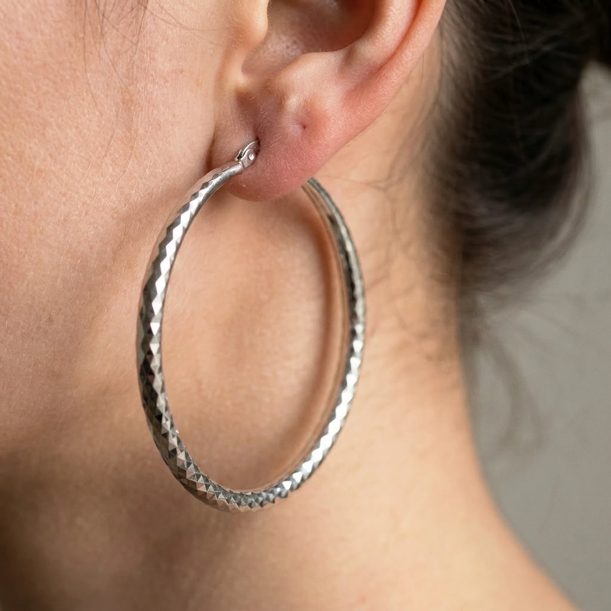 Silver tone stainless steel diamond cut large hoop earrings, macro detail on the earlobe | SKU: AUR-DCTHOP-S