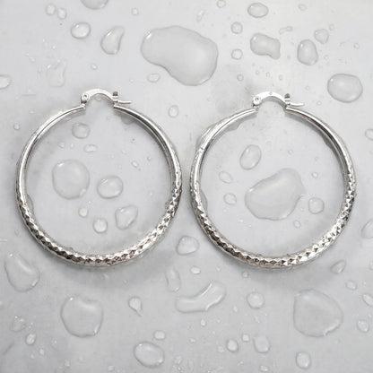 Silver tone stainless steel diamond cut large hoop earrings, still life on a wet surface, waterproof | SKU: AUR-DCTHOP-S
