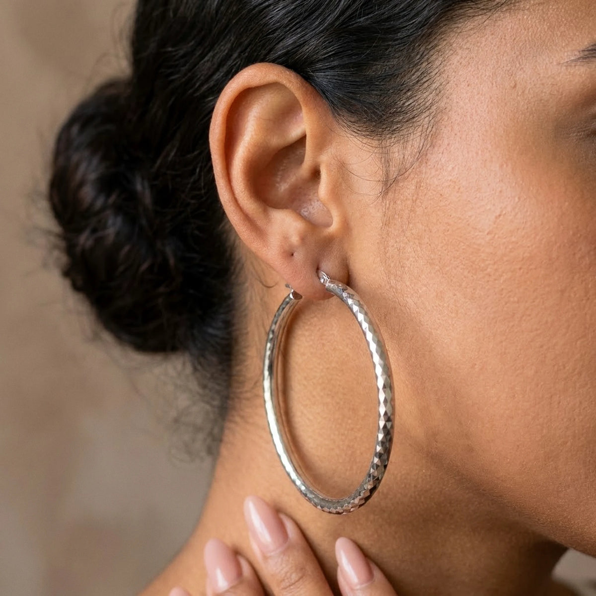 Silver tone stainless steel diamond cut large hoop earrings, worn close up on the ear