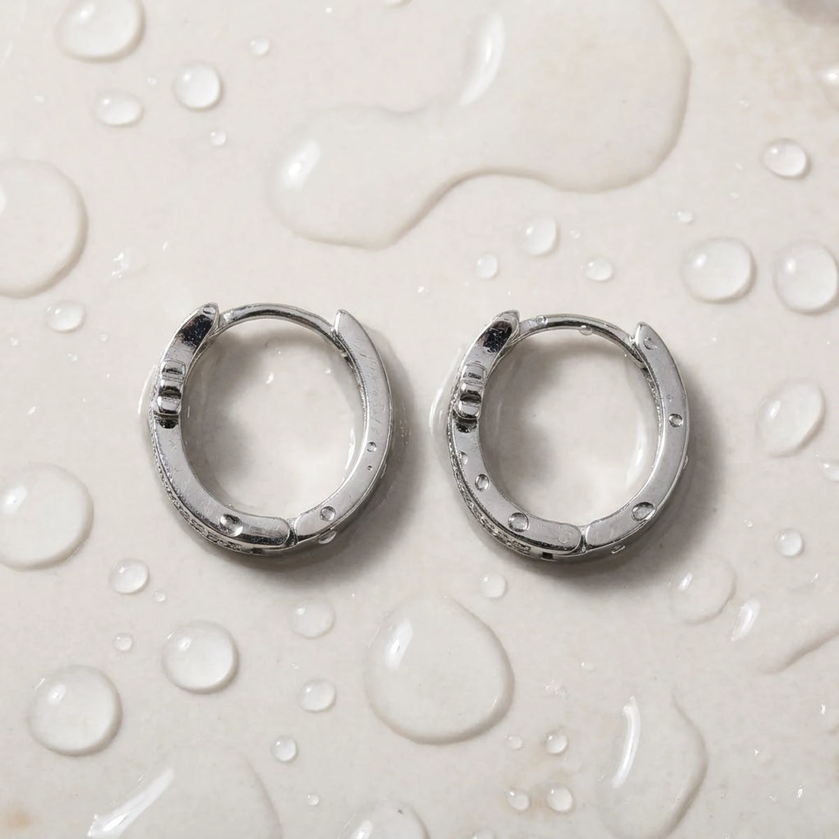 Silver tone stainless steel pave cross huggie hoop earrings, still life on a wet surface, waterproof | SKU: AUR-CRXHUG-S
