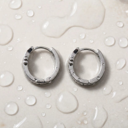 Silver tone stainless steel pave cross huggie hoop earrings, still life on a wet surface, waterproof | SKU: AUR-CRXHUG-S