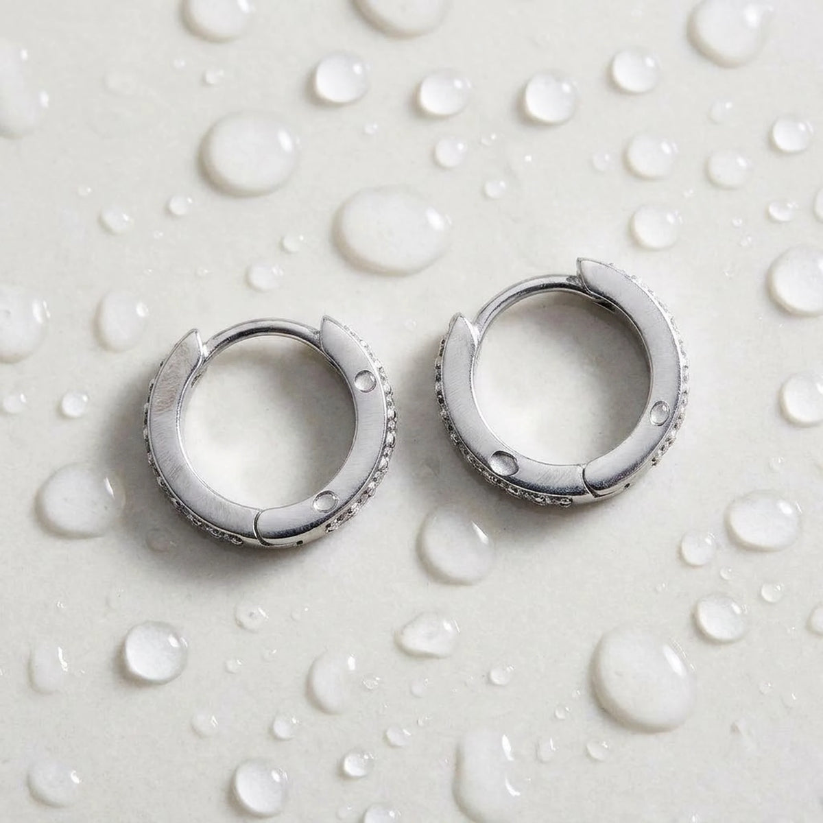 Silver tone stainless steel pave huggie hoop earrings, still life on a wet surface, waterproof | SKU: AUR-PVHUGG-S