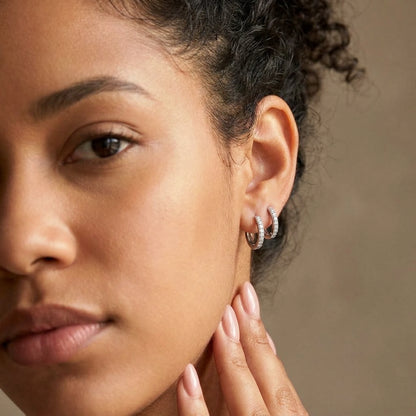 Silver tone stainless steel pave huggie hoop earrings, worn close up on the ear