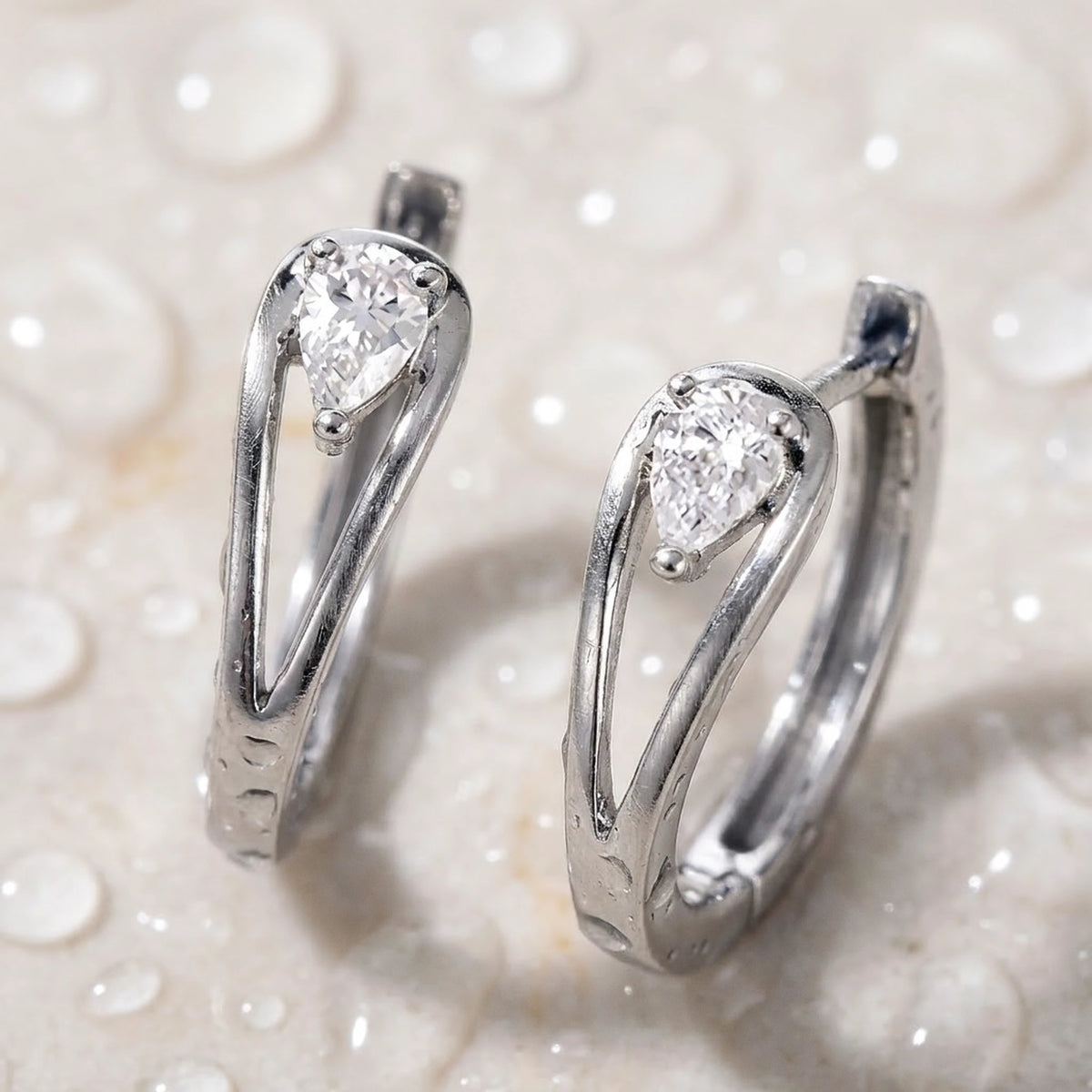 Silver tone stainless steel pear cut crystal huggie hoop earrings, still life on a wet surface, waterproof | SKU: AUR-PRCZHG-S
