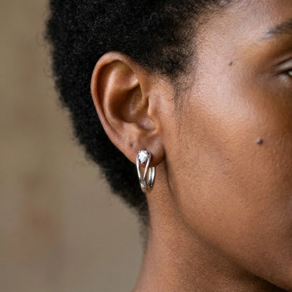 Silver tone stainless steel pear cut crystal huggie hoop earrings, worn close up on the ear