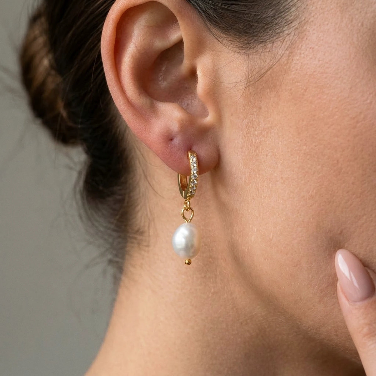 Silver tone stainless steel freshwater pearl drop huggie earrings, macro detail on the earlobe | SKU: AUR-PRLHUG-S