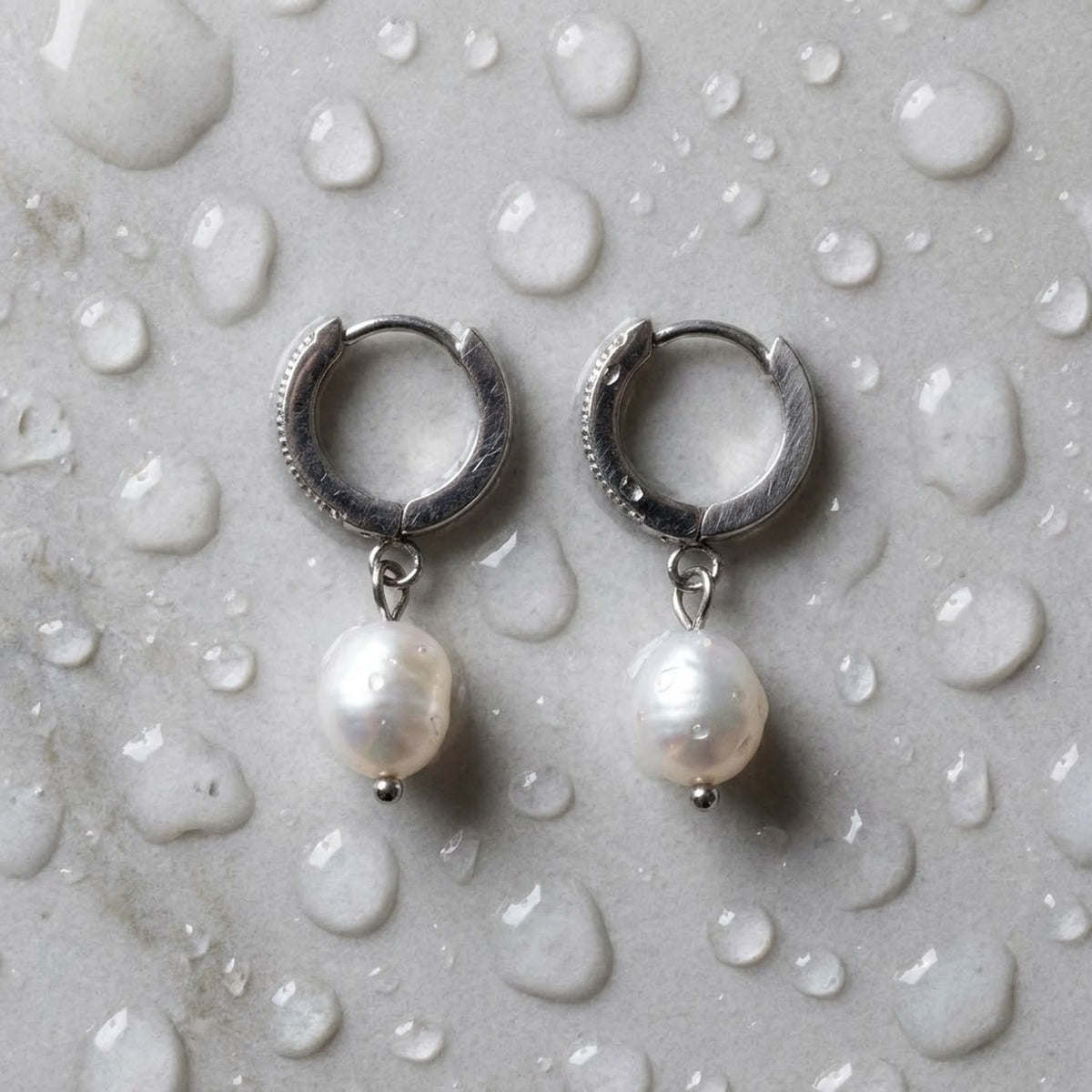 Silver tone stainless steel freshwater pearl drop huggie earrings, still life on a wet surface, waterproof | SKU: AUR-PRLHUG-S