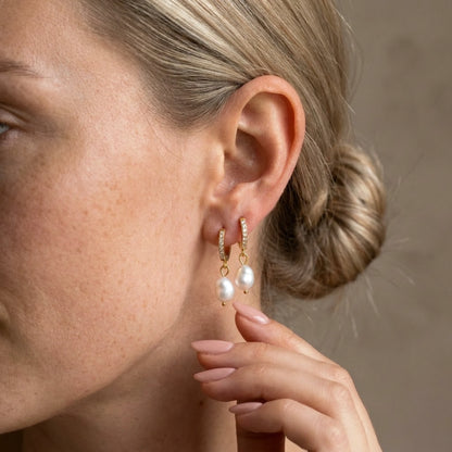 Silver tone stainless steel freshwater pearl drop huggie earrings, worn close up on the ear