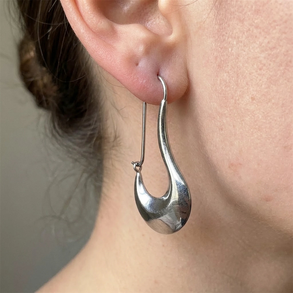 Silver tone stainless steel sculpted crescent drop earrings, macro detail on the earlobe | SKU: AUR-SCPCRS-S