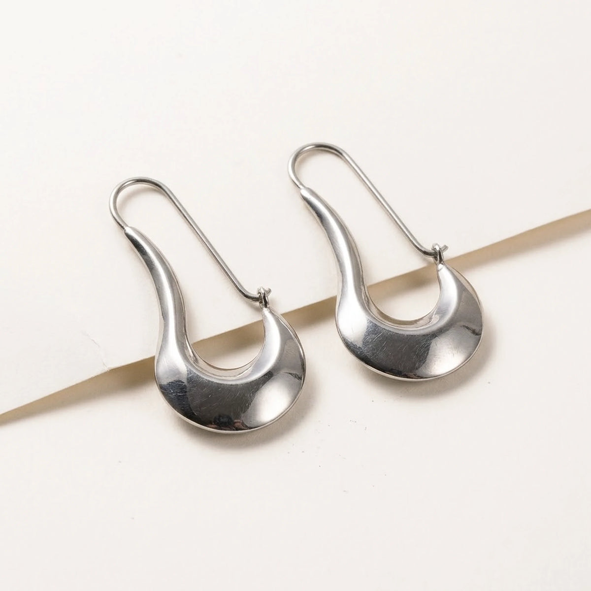Silver tone stainless steel sculpted crescent drop earrings, product shot on white | SKU: AUR-SCPCRS-S