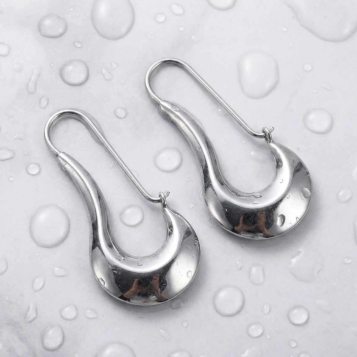 Silver tone stainless steel sculpted crescent drop earrings, still life on a wet surface, waterproof | SKU: AUR-SCPCRS-S
