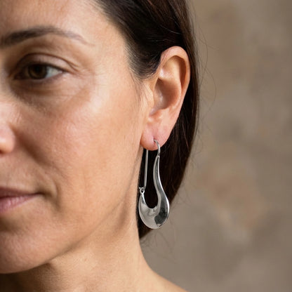 Silver tone stainless steel sculpted crescent drop earrings, worn close up on the ear