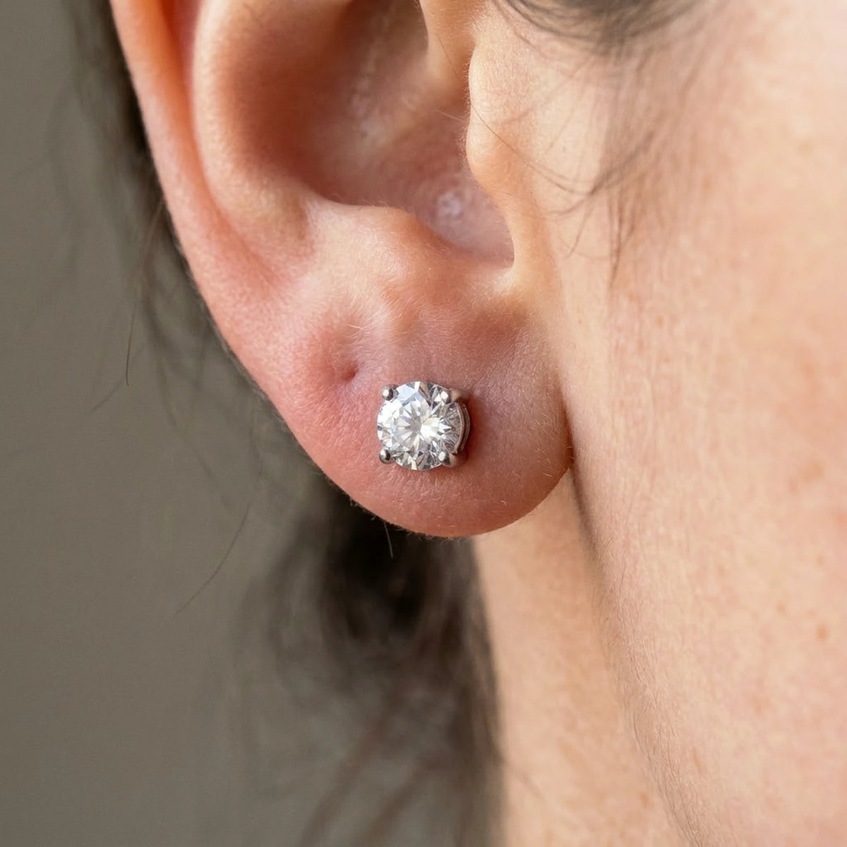 Silver tone stainless steel cubic zirconia solitaire stud earrings, macro detail on the earlobe | SKU: AUR-SOLSTD-S