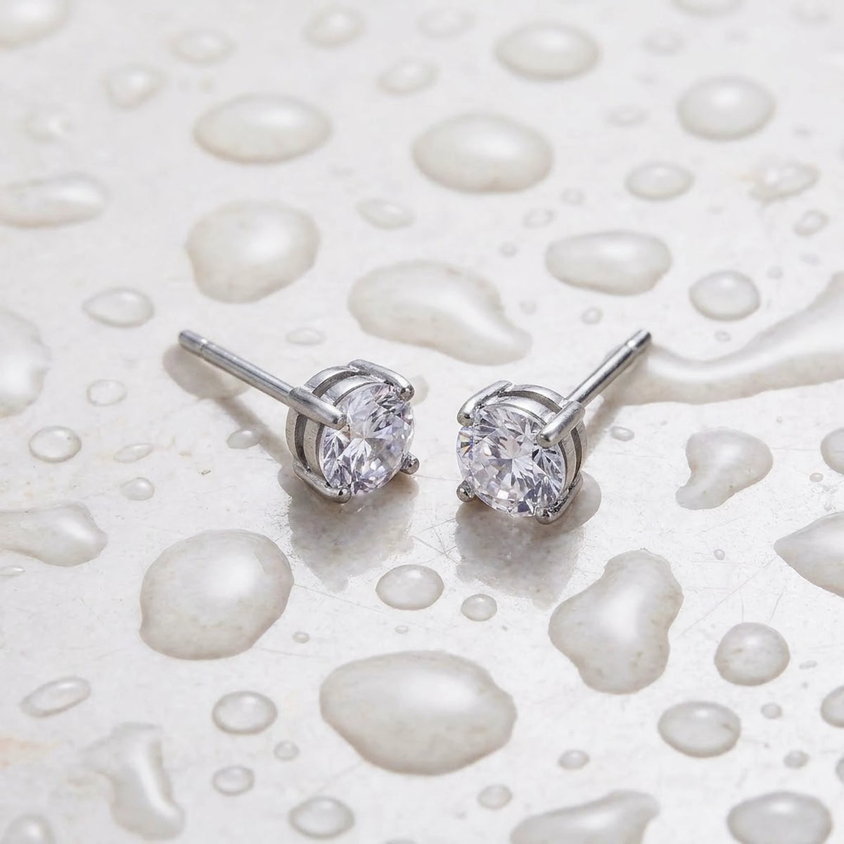 Silver tone stainless steel cubic zirconia solitaire stud earrings, still life on a wet surface, waterproof | SKU: AUR-SOLSTD-S