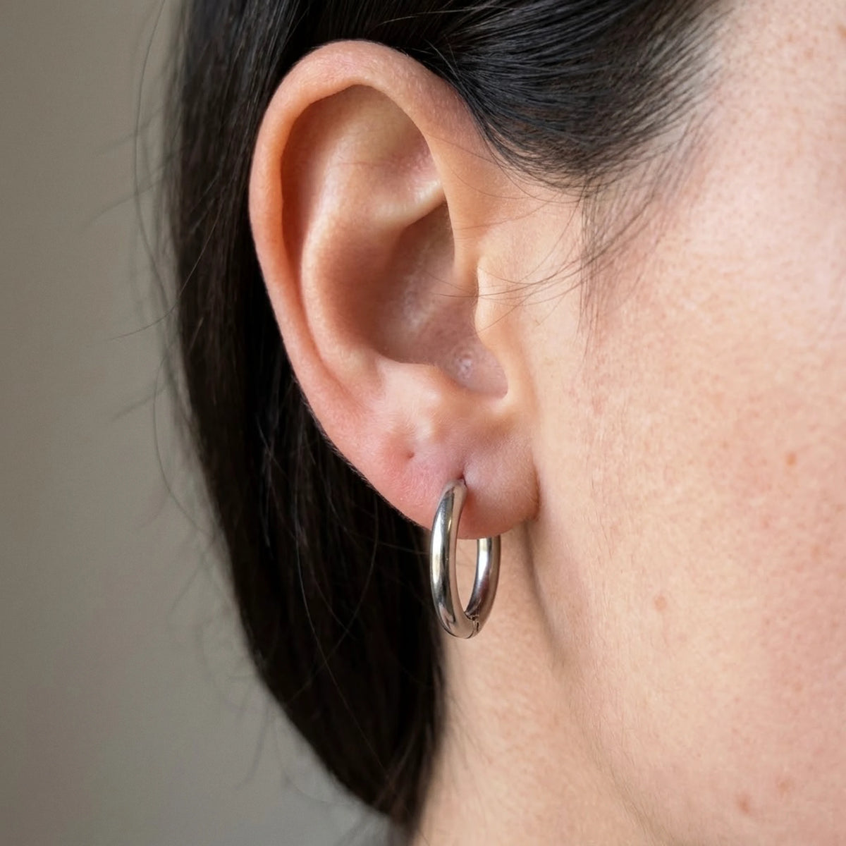 Silver tone stainless steel tiny huggie hoop earrings, macro detail on the earlobe | SKU: AUR-TNYHUG-S