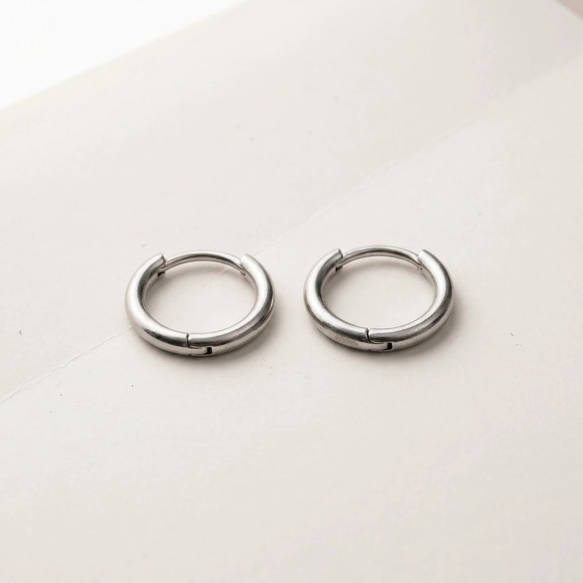 Silver tone stainless steel tiny huggie hoop earrings, product shot on white | SKU: AUR-TNYHUG-S
