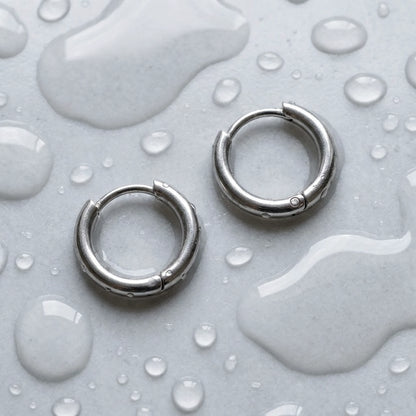 Silver tone stainless steel tiny huggie hoop earrings, still life on a wet surface, waterproof | SKU: AUR-TNYHUG-S