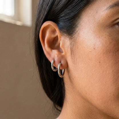 Silver tone stainless steel tiny huggie hoop earrings, worn close up on the ear