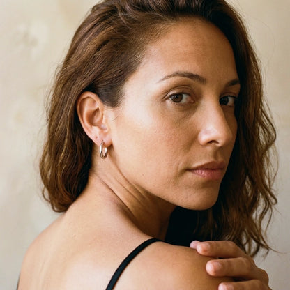 Silver tone stainless steel tiny huggie hoop earrings, worn, over the shoulder portrait | SKU: AUR-TNYHUG-S
