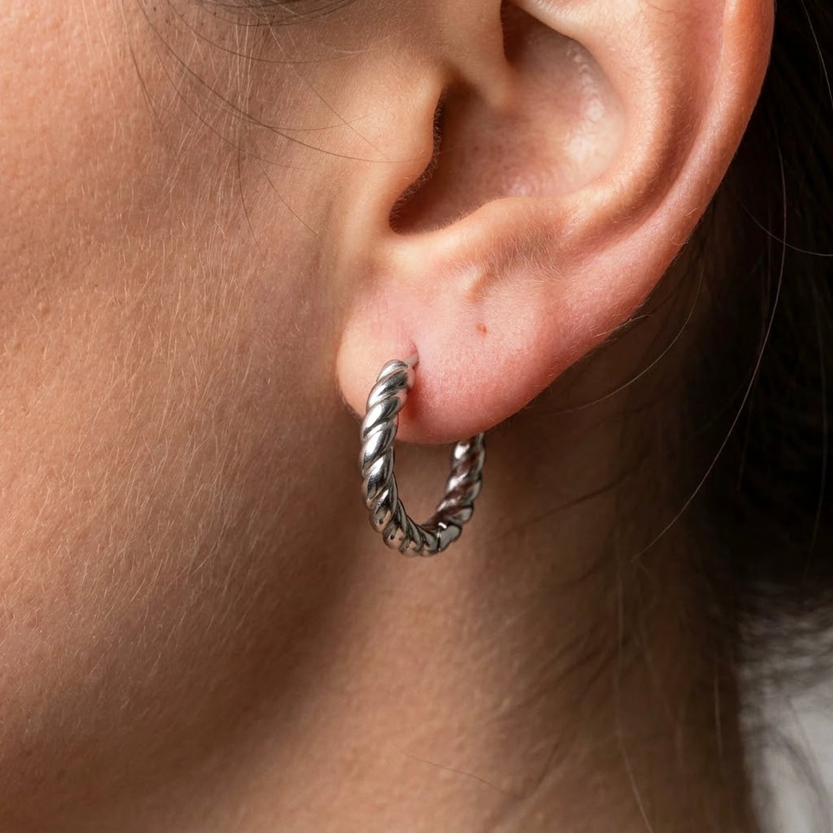 Silver tone stainless steel twisted rope huggie hoop earrings, macro detail on the earlobe | SKU: AUR-TWRHUG-S