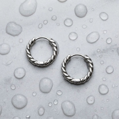 Silver tone stainless steel twisted rope huggie hoop earrings, still life on a wet surface, waterproof | SKU: AUR-TWRHUG-S