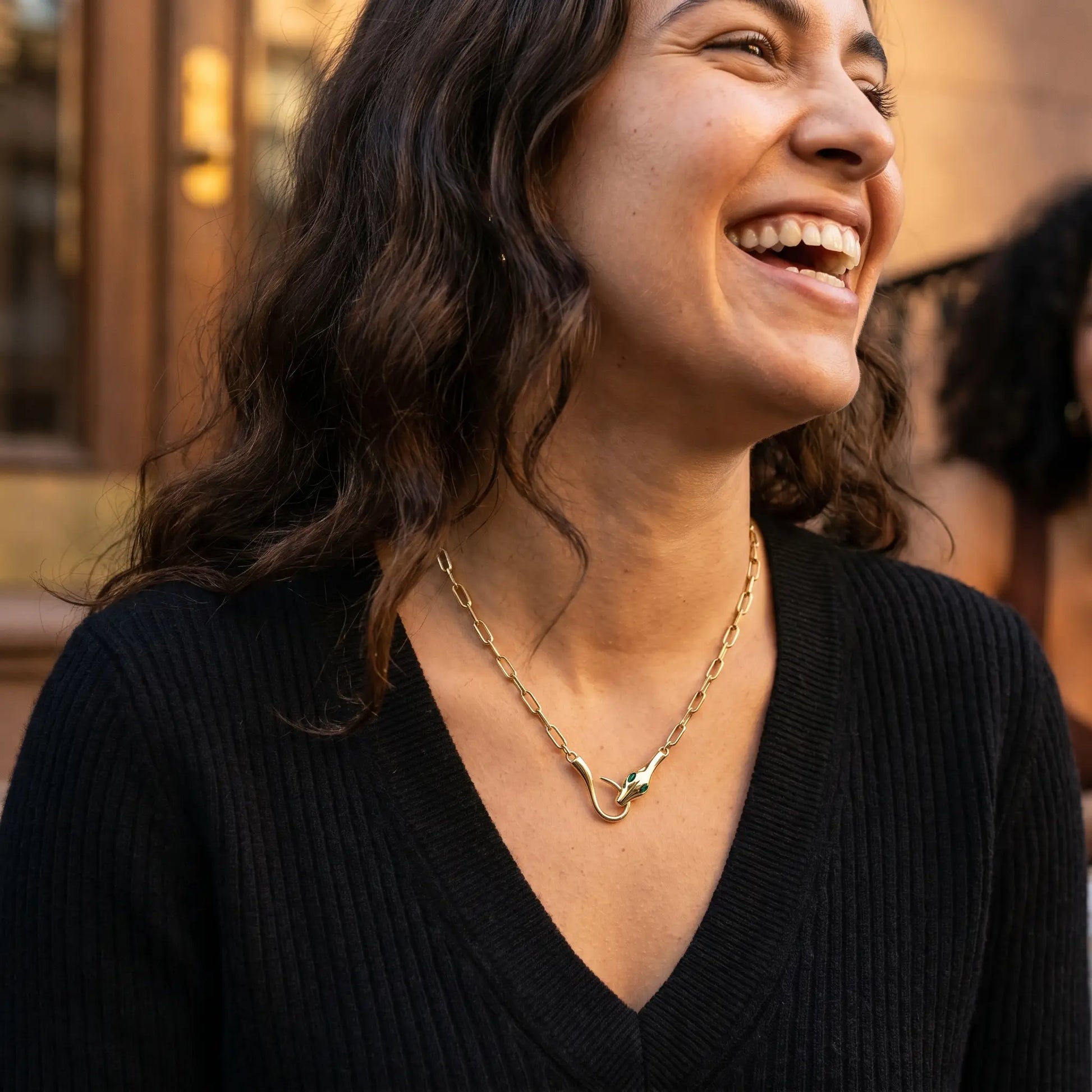 Snake pendant necklace candid joy lifestyle - golden hour NYC brownstone black sweater Latina laughing