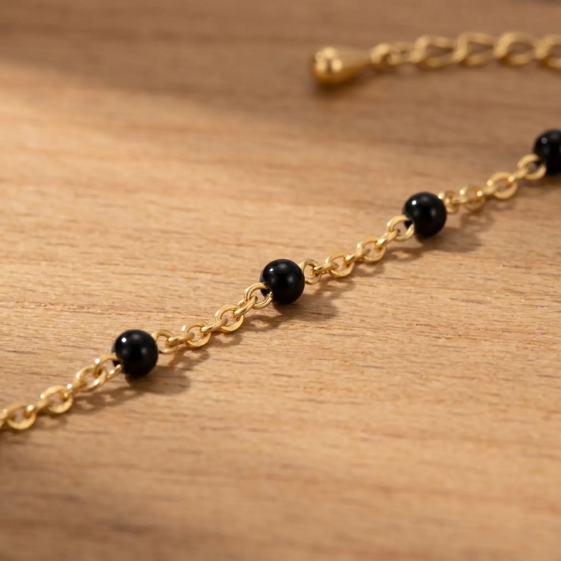 Macro detail of glossy black enamel beads on fine 18K gold cable chain anklet, polished onyx finish, artisan jewelry close-up