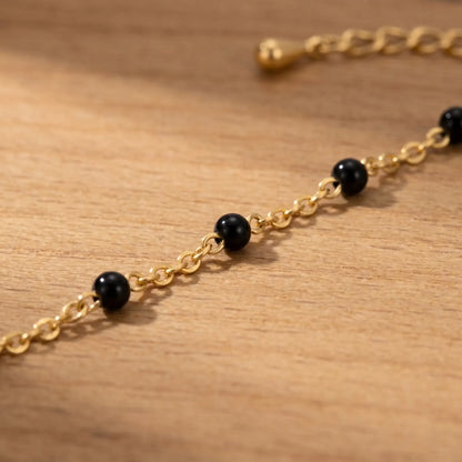 Macro detail of glossy black enamel beads on fine 18K gold cable chain anklet, polished onyx finish, artisan jewelry close-up
