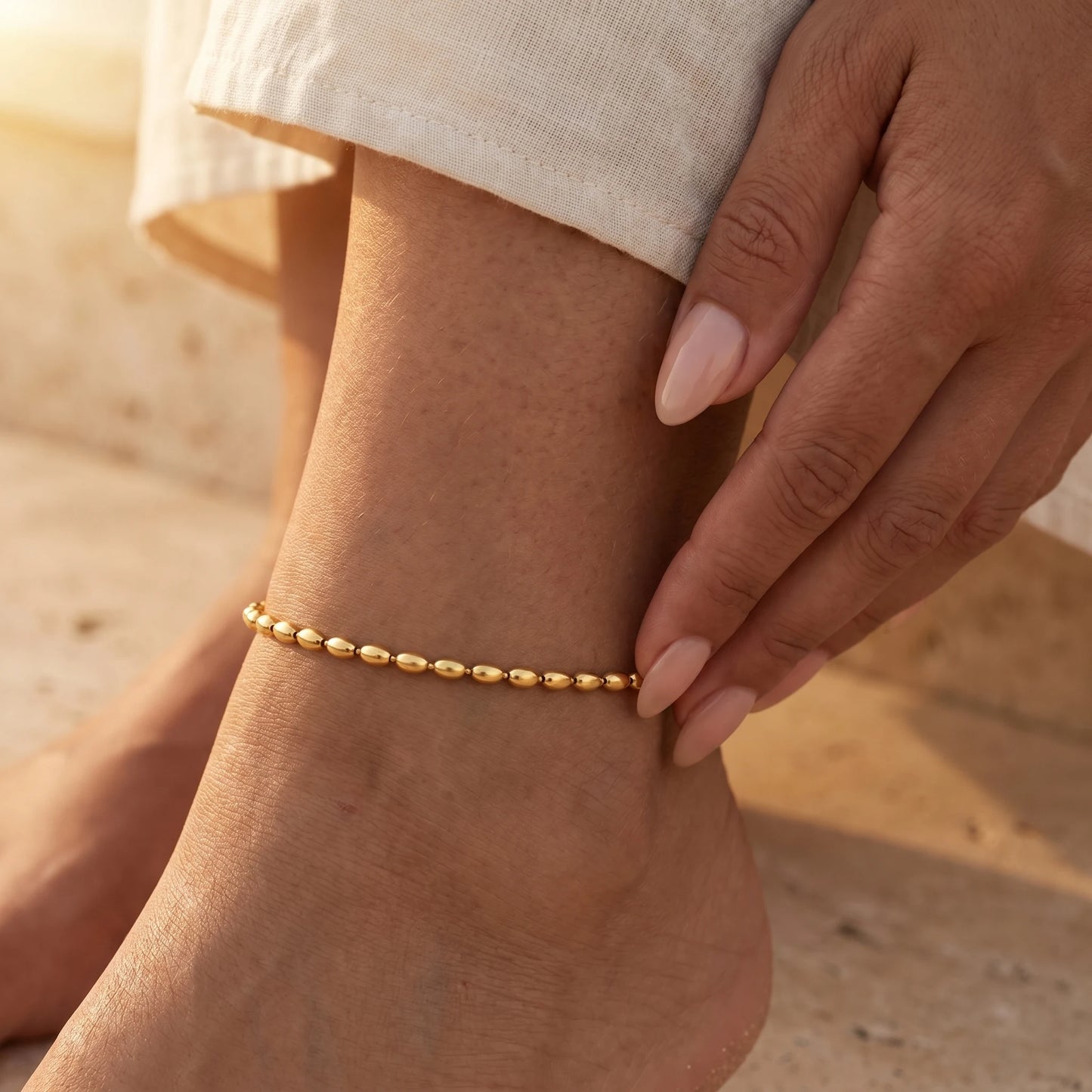 Hand touching gold oval bead anklet intimate close-up