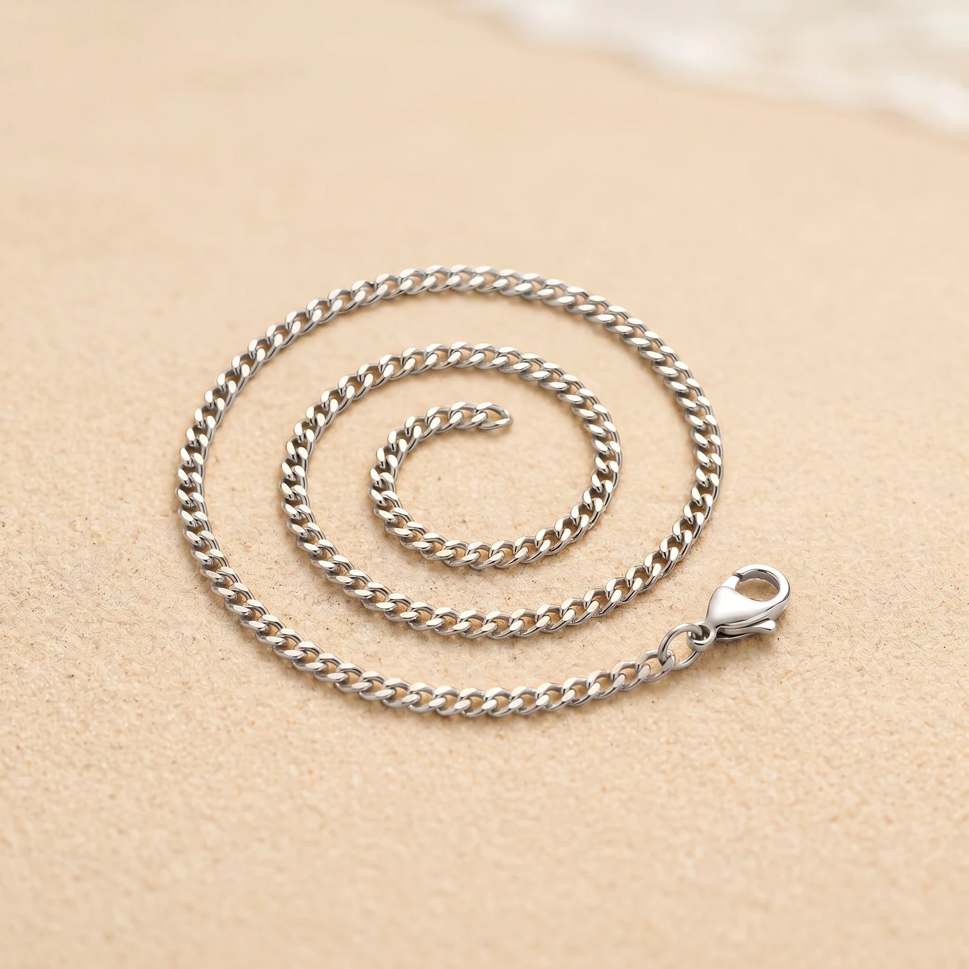 Silver 4mm curb-link anklet coiled packshot on warm sand