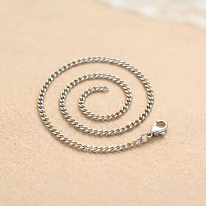 Silver 4mm curb-link anklet coiled packshot on warm sand