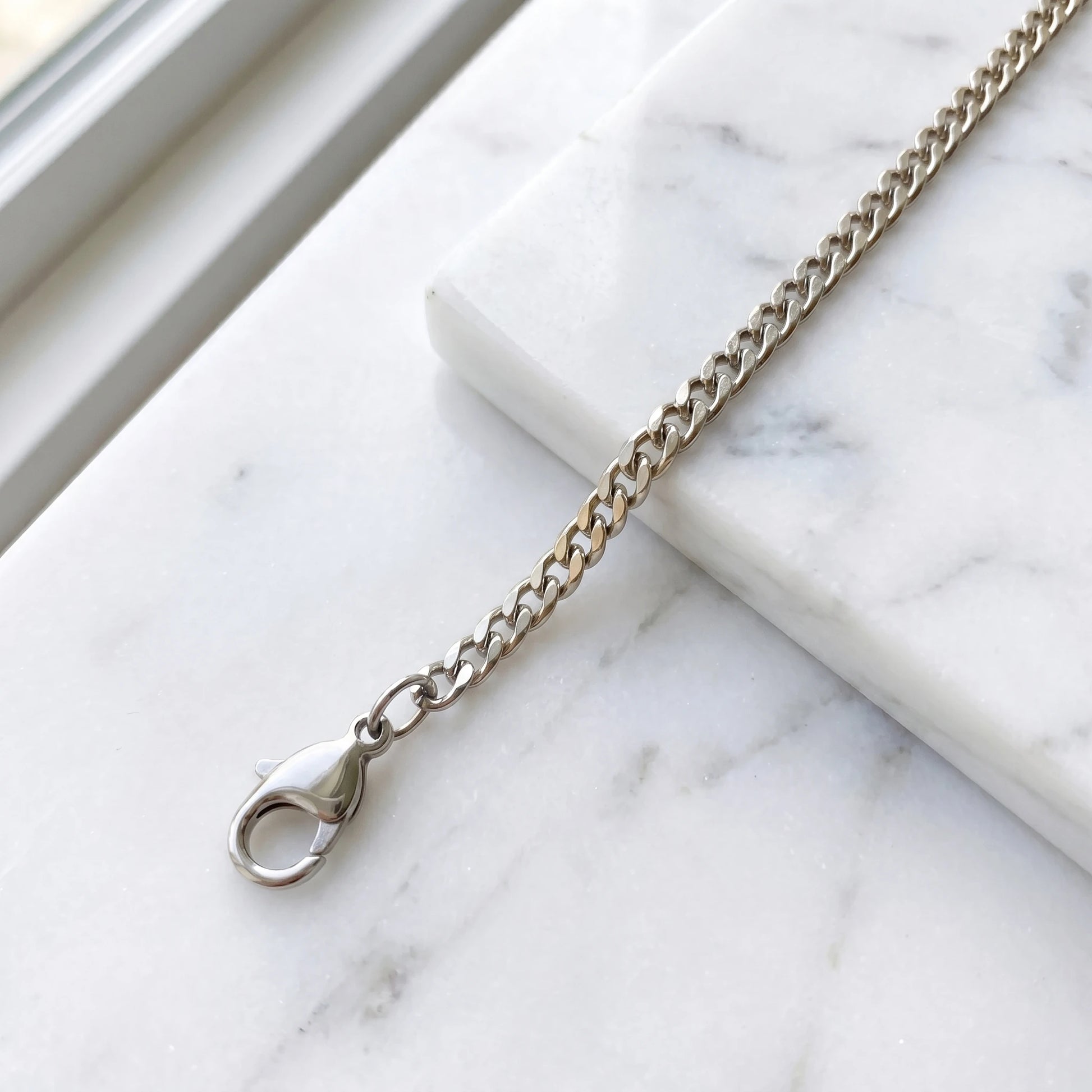 Silver 4mm curb-link anklet macro on white marble with lobster clasp